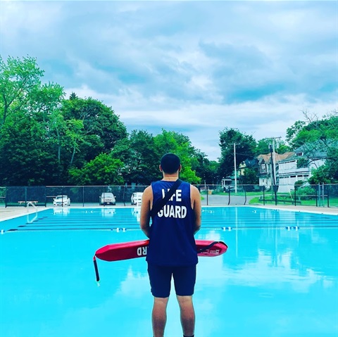 Lifeguard holding swim tube observes outdoor pool
