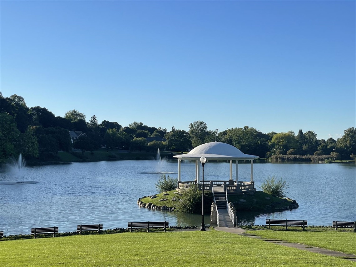A gazebo on a small island in a lake with a bridge leading to it